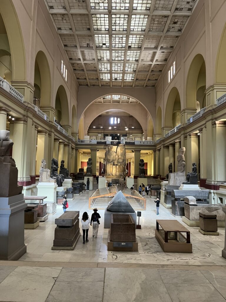 A view of the museum's grand Main Hall, featuring a soaring glass-paned ceiling and a vast collection of colossal sarcophagi and Old Kingdom monuments.