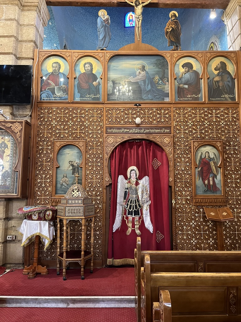 An intricately carved wooden iconostasis stands adorned with vibrant religious icons, reflecting the deep liturgical traditions of the Coptic Orthodox Church.