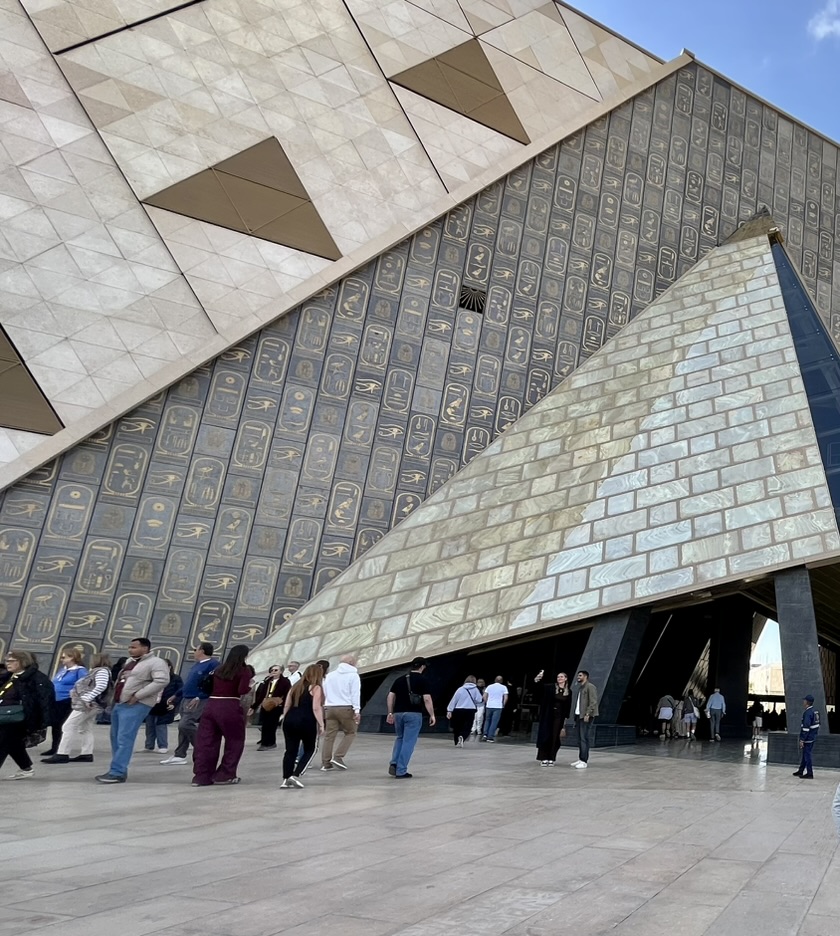 The museum’s exterior features a vast wall of translucent stone and glass adorned with thousands of pyramid-inspired triangles and royal cartouches, echoing the geometry of the ancient world.