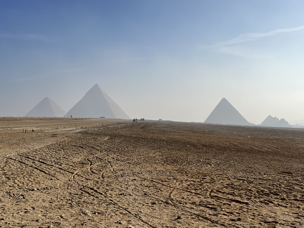 Traditional horse-drawn carriages, known as hantours, positioned in the desert sands near the Great Pyramid of Khufu during the early hour.