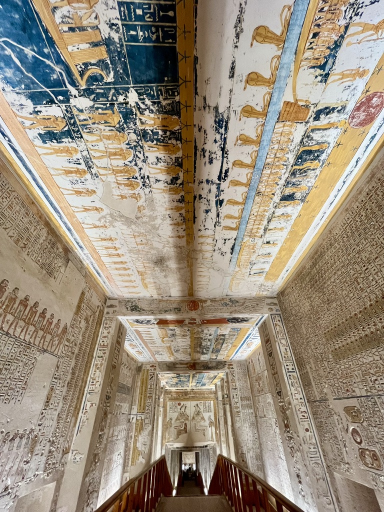A symmetrical view looking down the steeply inclined entrance corridor of the Tomb of Ramesses VI, featuring walls and ceilings entirely covered in vibrant astronomical and religious texts.