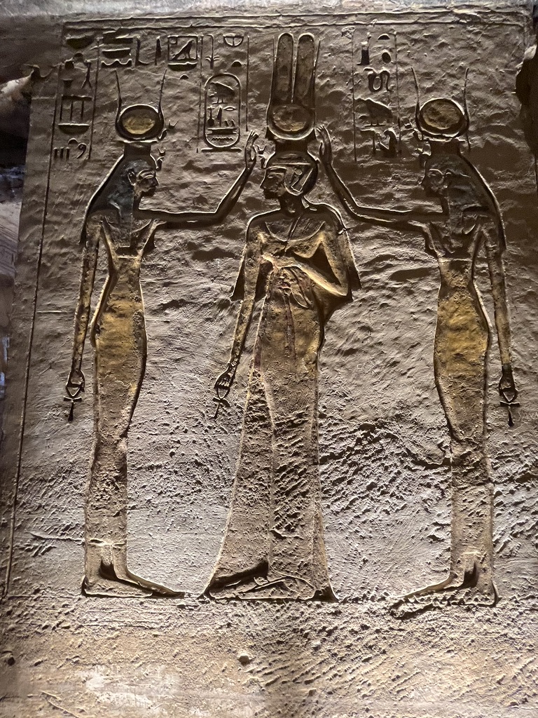 A beautifully preserved wall relief showing Queen Nefertari standing between the goddesses Isis and Hathor, who are placing a divine crown upon her head.