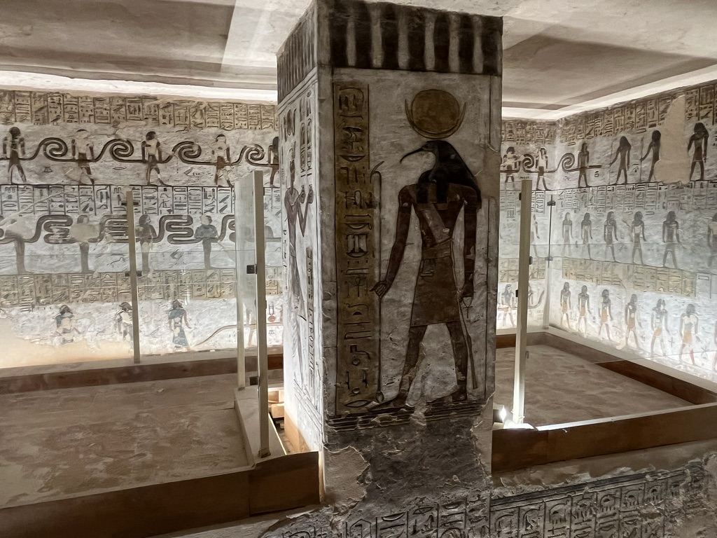 A detailed relief on a central support pillar depicting a protective deity standing alongside vertical registers of hieroglyphic funerary spells.