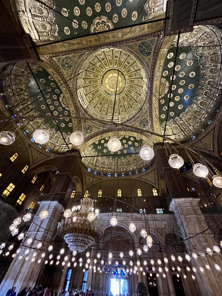 The vast prayer hall of the Mosque of Muhammad Ali, featuring a massive central chandelier and concentric circles of smaller lamps suspended from the Ottoman-style dome.