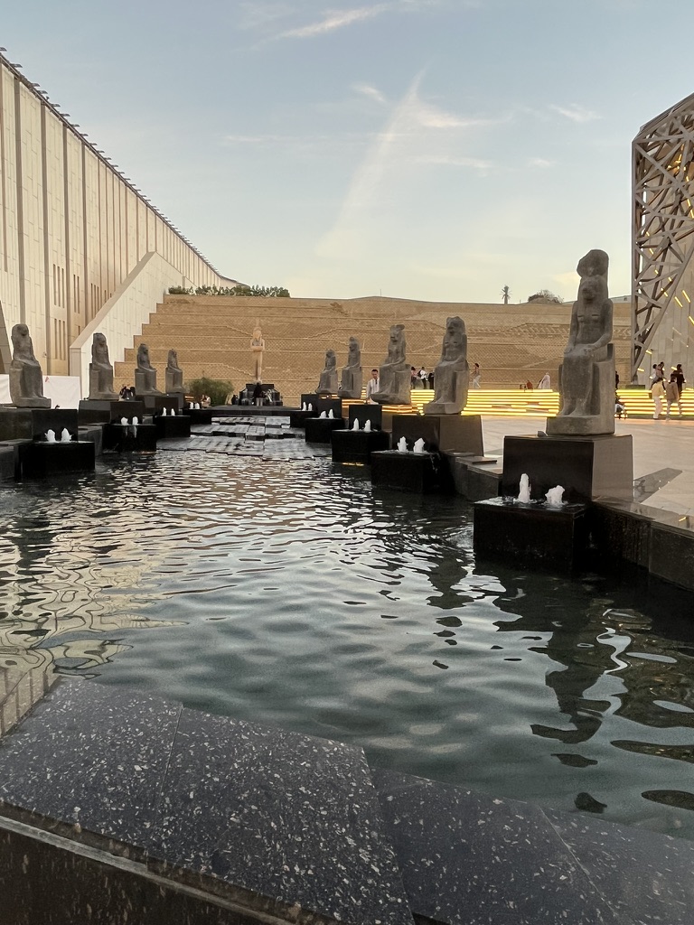A row of granite statues of the goddess Sekhmet lining an outdoor water feature.