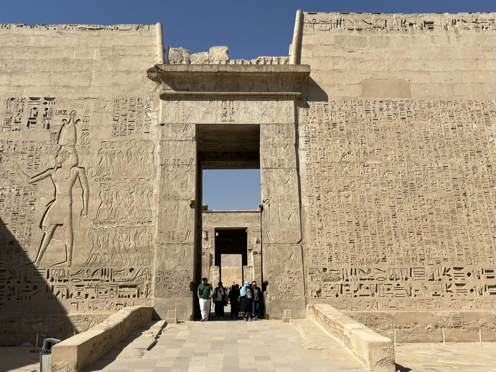 The monumental First Pylon of Medinet Habu, featuring a massive relief of Pharaoh Ramesses III smiting his enemies in the presence of the god Amun-Re.