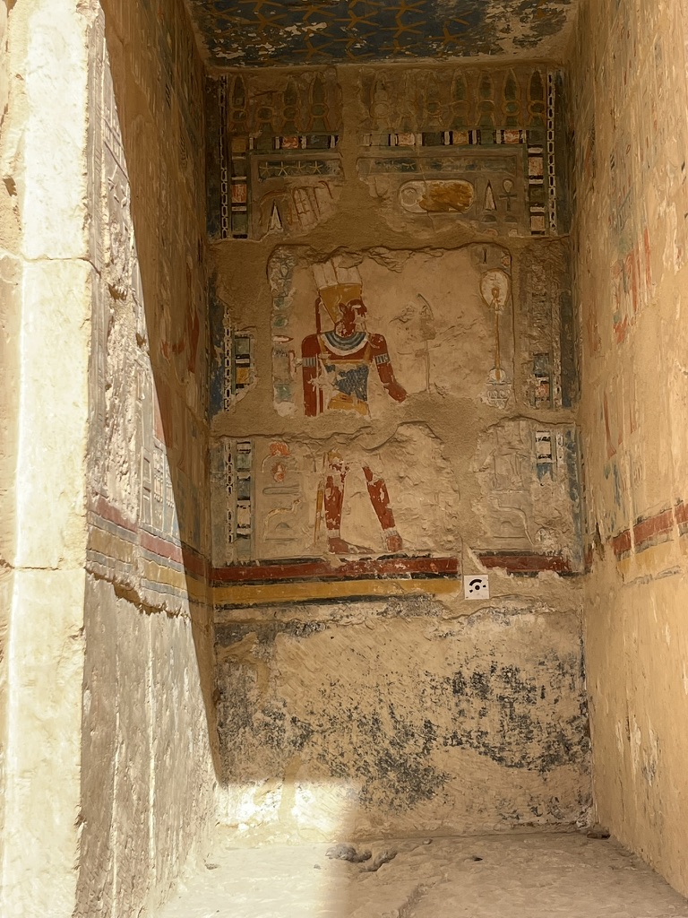 Exceptionally well-preserved polychrome reliefs on an interior wall, depicting the queen making offerings to the gods under a ceiling decorated with yellow stars on a blue background.