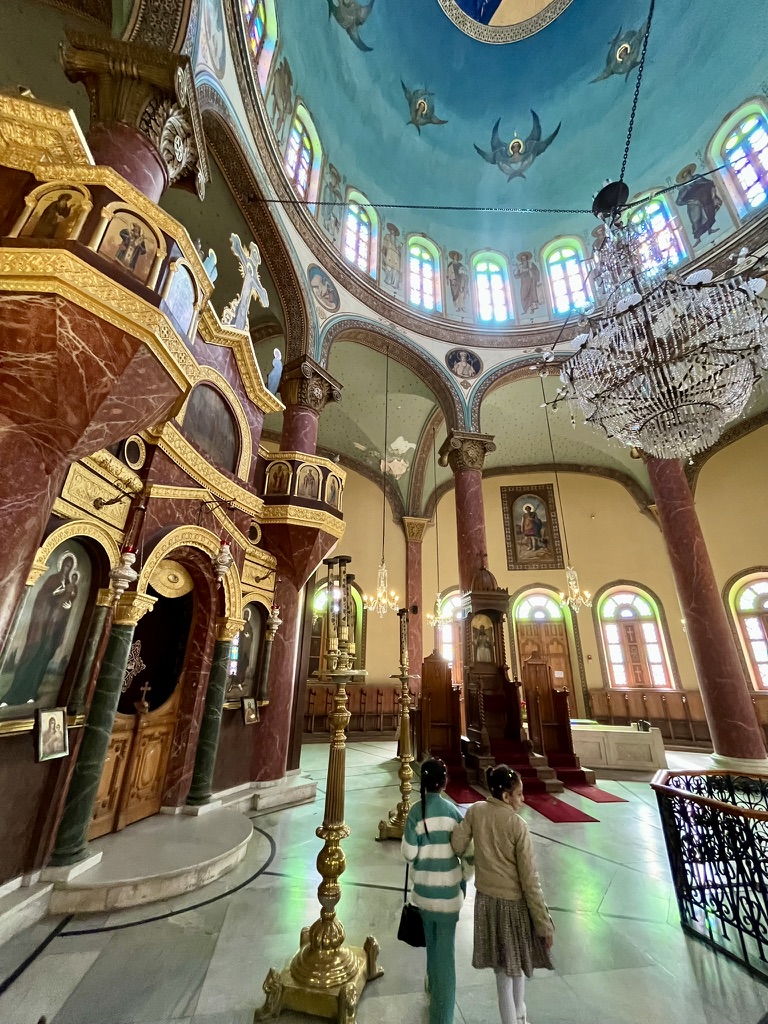 Two young visitors walking before the ornate wooden iconostasis and marble columns of the Church of Saint Barbara, one of the oldest and largest Coptic churches in Egypt.