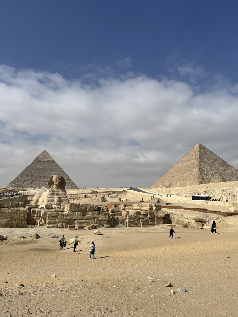 Egypt Itinerary Options: A wide-angle view of the Great Sphinx of Giza in the foreground, with the Pyramids of Khufu and Khafre positioned behind it under a partially cloudy sky.