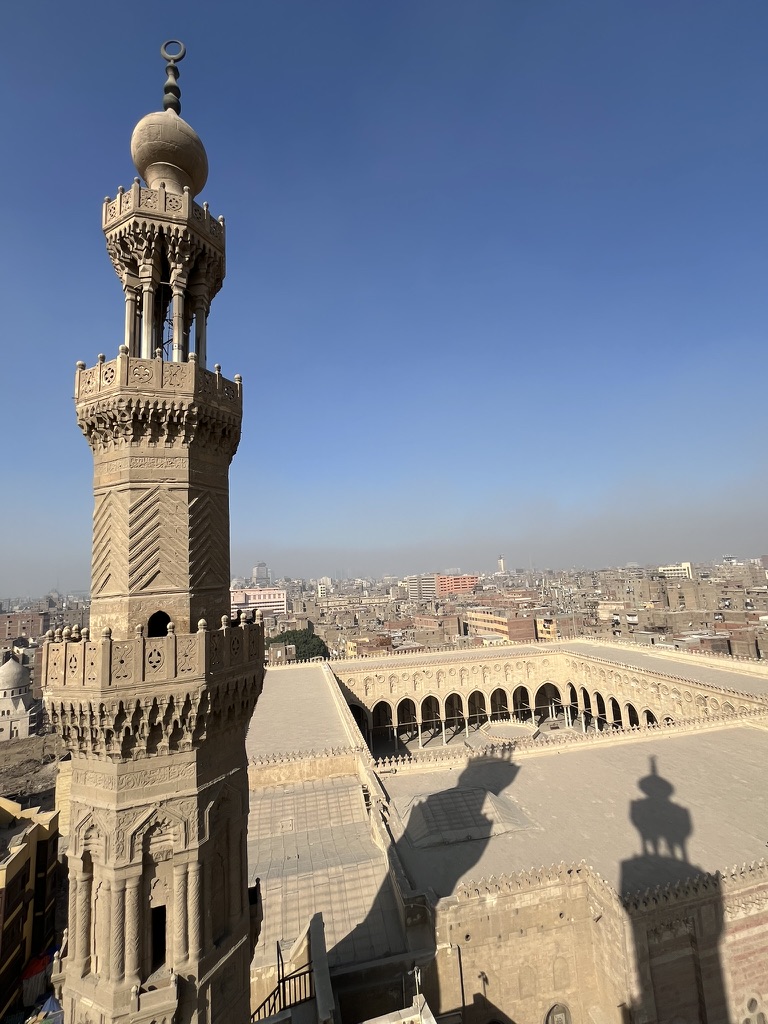 Shadows of History: An aerial perspective from Bab Zuweila, perfectly framed by an intricate stone minaret and the vast urban horizon.