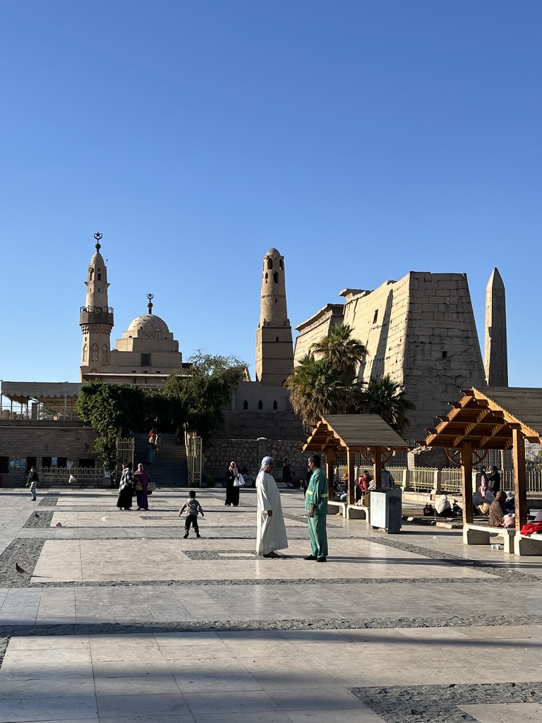 Local residents and visitors gathered in the public square adjacent to the Luxor Temple, with the minarets of the 13th-century Mosque of Abu al-Haggag rising above the ancient pylon walls.