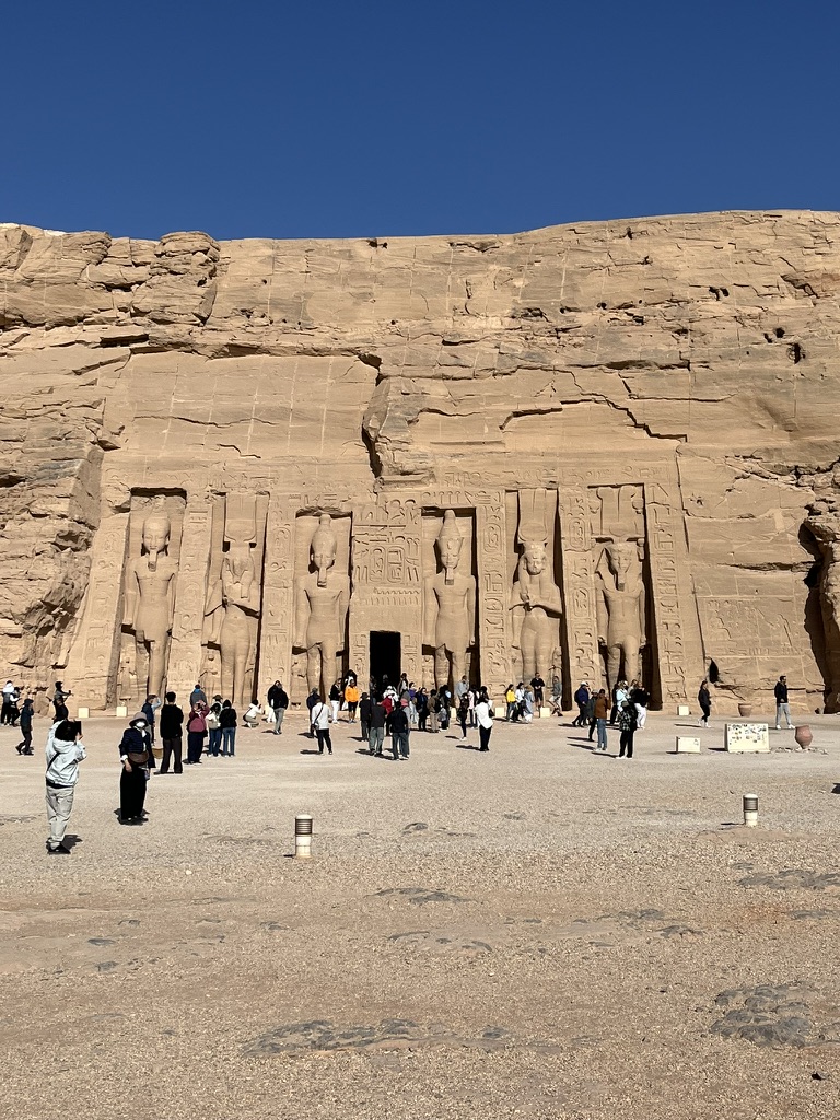 A wide view of the six standing statues carved into the cliff face, featuring Queen Nefertari flanked by her husband, Pharaoh Ramesses II.