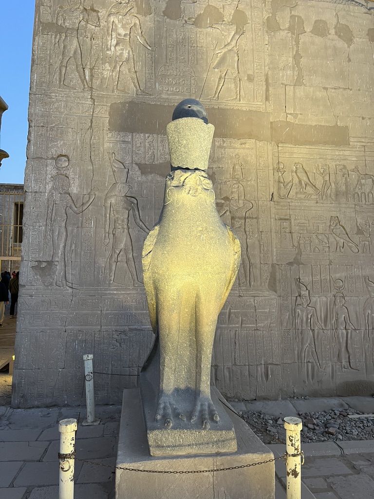 The monumental First Pylon, standing 36 meters tall, guarded by the iconic granite statue of Horus the Falcon wearing the Double Crown of Egypt.